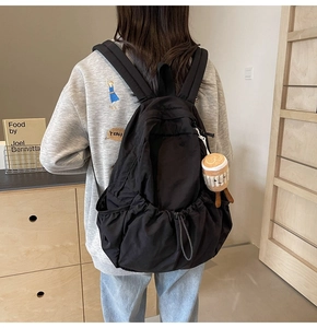 Detail of black nylon backpack on model with coffee cup plush pendant charm