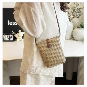 Close-up of woven straw crossbody bag featuring dark wooden button and thin leather strap