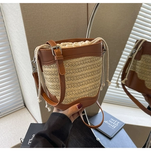 Close-up of woven straw bucket bag with brown leather trim and adjustable strap