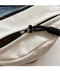 Detail of silver metal zipper pull with black woven cord on white canvas crossbody bag