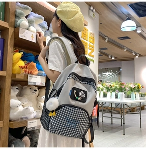 Casual grey and black checkered backpack with a cute white pompom charm on a model