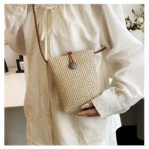 Straw woven crossbody phone bag with brown leather strap worn over a white dress
