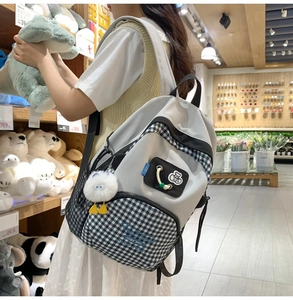 Detail of grey checkered backpack with cute plush charm and cartoon badges shown in a store