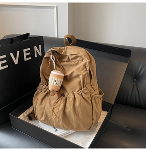 Detail of a brown waterproof nylon backpack featuring a drawstring pocket and cute plush charm