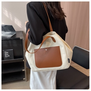 Detailed view of canvas tote bag with brown leather handles and side brand tag detail