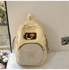 Detailed view of cream nylon backpack with biscuit patch and embroidered text on fabric