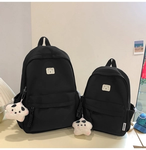 Detail of two-piece black nylon backpacks with square bear patch and white star plush charms