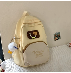 Close-up of a cute cream and yellow backpack featuring a cookie patch and plush charm
