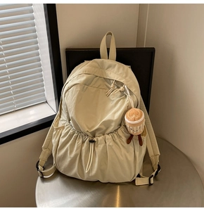 Close-up of beige nylon backpack featuring drawstring pocket and plush coffee cup charm