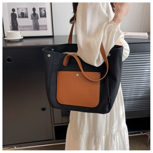 Detail of black canvas tote with brown leather pocket and slim shoulder straps