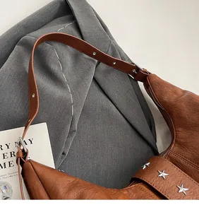 Détail d'un sac à bandoulière en cuir marron avec rivets étoiles argentés et bandoulière lisse