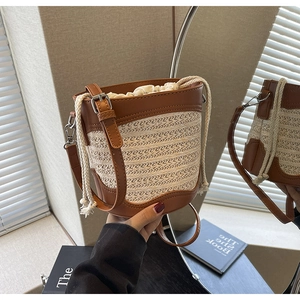 Detail of a woven straw bucket bag with brown leather trim and drawstring inner bag