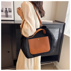 Detail view of the black canvas tote bag with brown leather pocket and adjustable shoulder straps