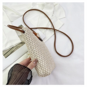 Detail of straw woven crossbody bag with brown strap and bead closure on a white blazer