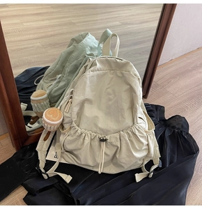 Detail of a beige nylon backpack featuring drawstring closure and a cupcake plush charm