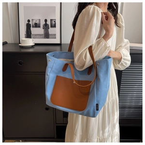 Detail view of sky blue canvas tote bag with brown leather pocket and straps on a model