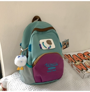 Detail of green nylon backpack featuring contrast purple pocket and plush bird charm