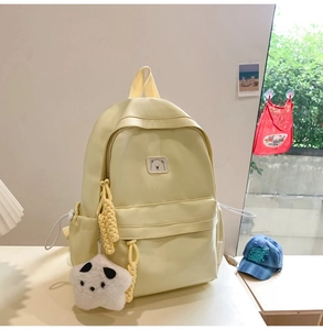 Detail shot of a yellow backpack featuring a cute bear patch and plush star pendant charm