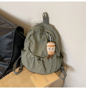 Detailed view of olive green backpack with drawstring closure and plush cup pendant