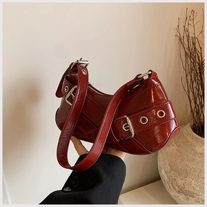 Close-up of a dark red glossy crescent bag with retro silver buckles and metal eyelets