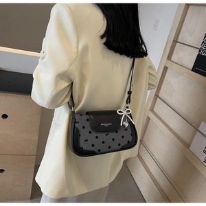 Detail of crossbody bag with pearl bow charm and heart pendant worn with a blazer