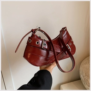 Close-up of deep red glossy leather shoulder bag with silver grommet details and buckles