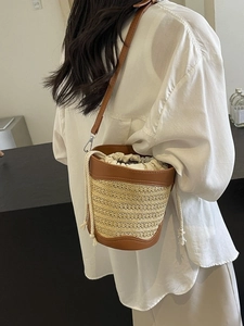 Straw weave bucket bag with brown leather trim and adjustable crossbody strap on model