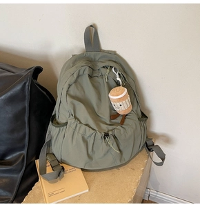 Detail of olive green nylon backpack with drawstring front pocket and plush coffee charm