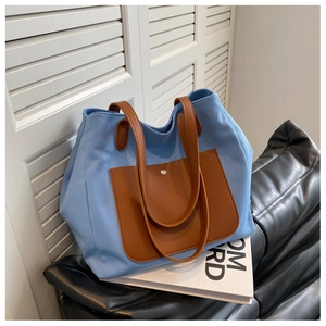 Detail of light blue canvas tote bag with brown leather pocket and metal snap closure