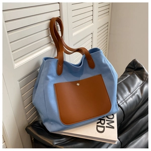 Detail of blue canvas tote bag featuring brown leather pocket and metallic button