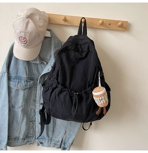 Detail of black nylon backpack with drawstring and plush charm hanging on a wall