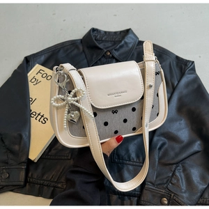 Detail of cream and gray polka dot bag with pearl bow and heart charm on black leather