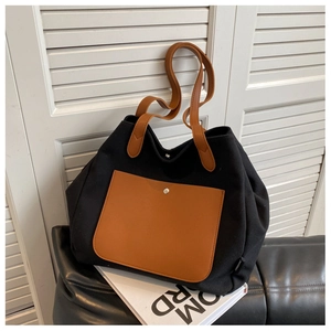 Detail of canvas tote bag showing black fabric texture and brown leather front pocket
