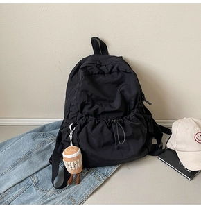 Detail of black nylon backpack featuring a cute coffee cup plush charm and drawstring pocket