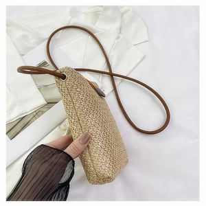 Detail of minimalist beige straw woven crossbody bag with brown strap and button closure