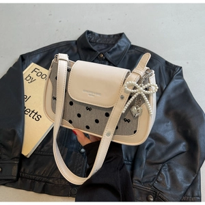 Detail of cream leather bag featuring gray canvas, black dots, and heart pearl pendants