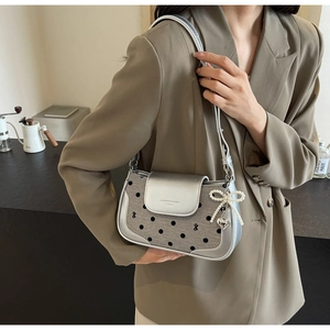 Detail of silver polka dot underarm bag with pearl bow and heart charm on a model