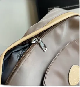 Detailed close-up of smooth silver metal zipper and brand logo on khaki nylon backpack