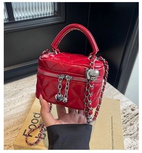 Close-up of red quilted mini box bag with heart-shaped zipper and metal chain strap