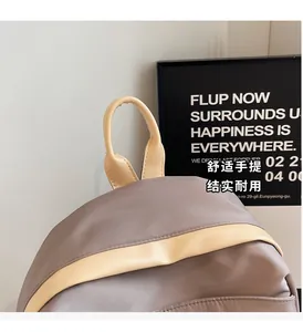 Detail view of the gray nylon backpack showing beige leather handle and stitching