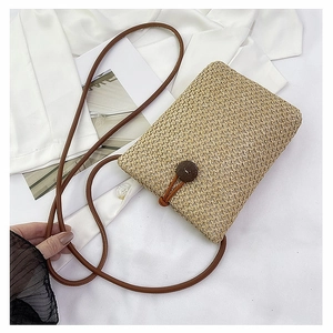 Detail of woven straw crossbody phone bag with brown strap and wooden button closure