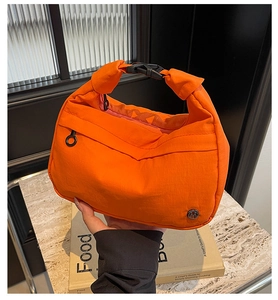 Détail du sac bandoulière orange avec boucle réglable et logo métallique M