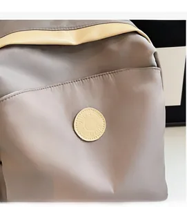 Detailed close-up of grey nylon backpack with beige leather accents and embossed logo patch