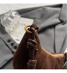 Close-up of brown suede bag with gold ring hardware and leather knot zipper detail