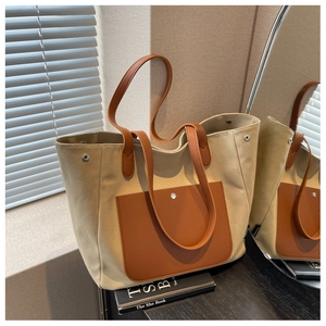 Detail view of beige canvas tote bag with brown leather pocket and metal side snaps