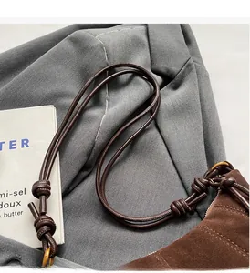 Detail of dark brown suede bag featuring woven shoulder strap and metal hardware