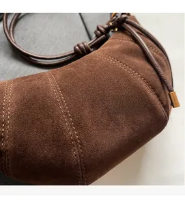 Detail of brown suede croissant bag showing parallel decorative stitching and gold metal accents