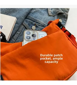 Détail du sac bandoulière orange en nylon avec poche avant pour le rangement du smartphone