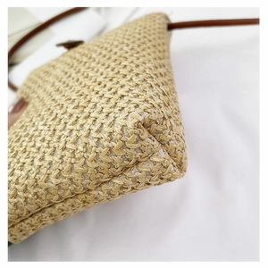 Detail of woven straw bag bottom showing tight texture and brown leather shoulder strap