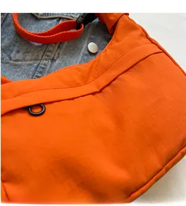 Détail d'un sac bandoulière orange avec texture ripstop et sangle réglable sur fond en jean
